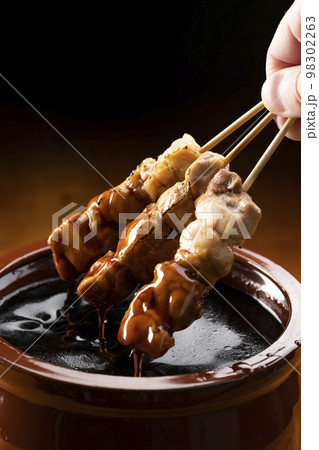 鶏のモモ肉の串焼きをタレ壺の中の焼き鳥のタレに漬ける 98302263