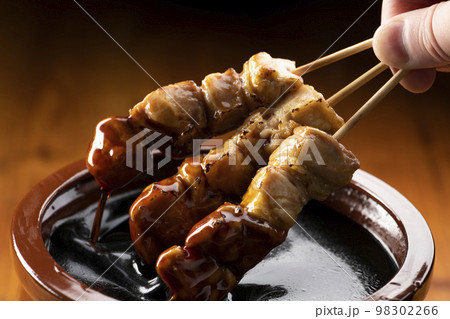 鶏のモモ肉の串焼きをタレ壺の中の焼き鳥のタレに漬ける 鶏のモモ肉の串焼きをタレ壺の中の焼き鳥のタレに漬ける 98302266