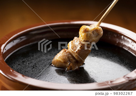 鶏のモモ肉の串焼きをタレ壺の中の焼き鳥のタレに漬ける 98302267