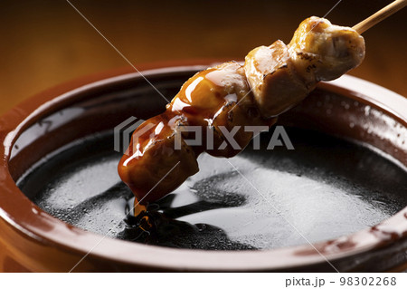 鶏のモモ肉の串焼きをタレ壺の中の焼き鳥のタレに漬ける 鶏のモモ肉の串焼きをタレ壺の中の焼き鳥のタレに漬ける 98302268