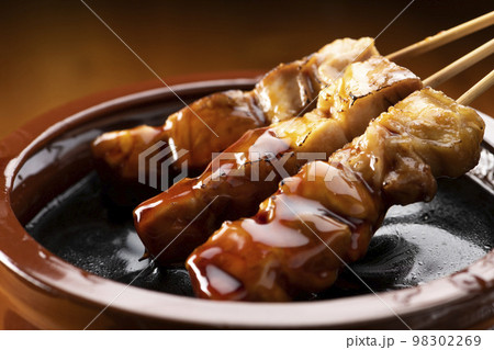 鶏のモモ肉の串焼きをタレ壺の中の焼き鳥のタレに漬ける 98302269