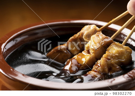 鶏のモモ肉の串焼きをタレ壺の中の焼き鳥のタレに漬ける 鶏のモモ肉の串焼きをタレ壺の中の焼き鳥のタレに漬ける 98302270