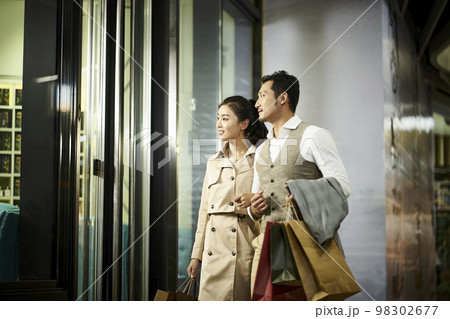 happy young asian couple looking into window of a shop in shopping mall 98302677
