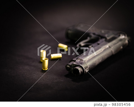 Handgun with 9mm shell casings on black background 98305456