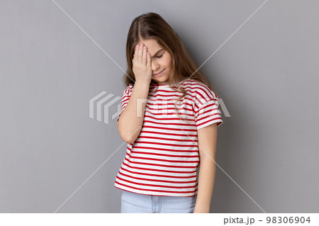 Oh no, I forgot. Portrait of little girl wearing striped T-shirt making facepalm gesture, feeling regret and shame about forgotten event, bad memory. Indoor studio shot isolated on gray background. Oh no, I forgot. Portrait of little girl wearing striped T-shirt making facepalm gesture, feeling regret and shame about forgotten event, bad memory. Indoor studio shot isolated on gray background. 98306904