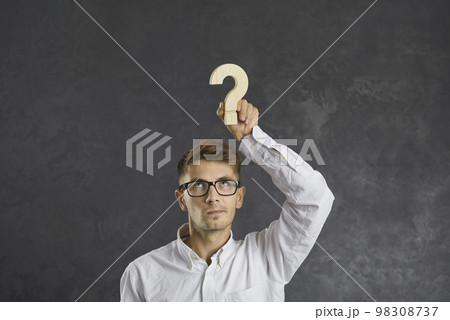 Embarrassed businessman with emotion of doubt on his face holding wooden question mark over his head 98308737