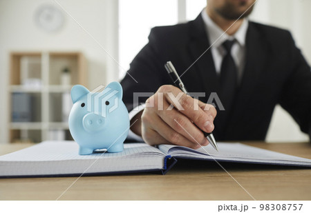 Piggy bank on the office desk of a businessman planning budget and writing in a notebook 98308757