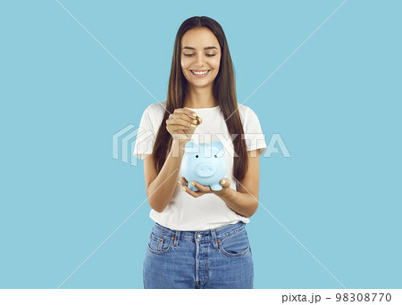 Portrait of happy woman who puts coin in piggy bank, saving money for purchase she dreams of. 98308770