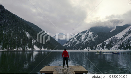 The guy standing on the pier admires mountain lake The guy standing on the pier admires mountain lake 98309102
