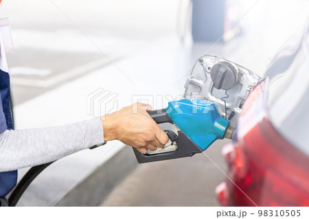 Hand of refueling worker are filling fuel to car in Petrol station. Focus on fuel nozzle and blur day light background 98310505