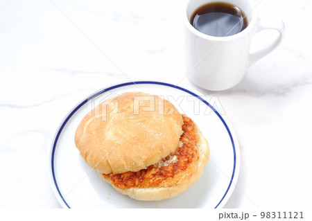 オーストリア発祥のロールパンのカイザーゼンメルにハムカツを挟んだサンドイッチとコーヒーの軽食をとる 98311121