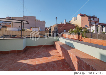 Big sunny terrace on the roof of modern building lined with red brick tiles overlooking the neighboring houses. Summer playground for leisure activities, party and meetings with friends. Big sunny terrace on the roof of modern building lined with red brick tiles overlooking the neighboring houses. Summer playground for leisure activities, party and meetings with friends. 98312915