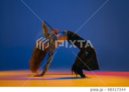 Flexible move. Young girl dancing heels dance in stylish clothes over blue background in neon with mixed lights. Concept of modern dance style Flexible move. Young girl dancing heels dance in stylish clothes over blue background in neon with mixed lights. Concept of modern dance style 98317344