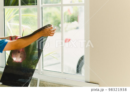 Woker wrapping tinting a house window with tinted foil using foggy spray. 98321938