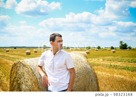 Happy farmer is standing beside bales of hay. He is examining st Happy farmer is standing beside bales of hay. He is examining st 98323168