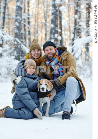 Portrait of happy family smiling at camera while walking with dog in winter forest 98324496