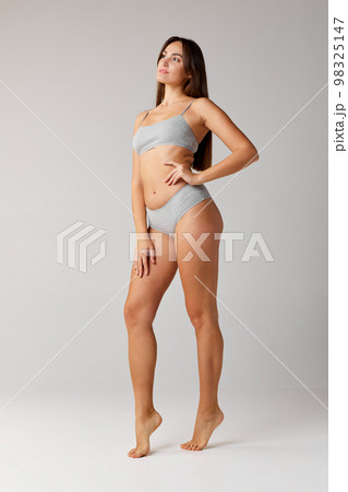 Self-care. Portrait of young beautiful girl with slim body posing in cotton underwear over grey studio background. Concept of body and skin care, fitness 98325147