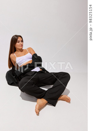 Fashion. Portrait of young beautiful girl posing in underwear and black classic suit over grey studio background. Concept of body and skin care, fitness 98325154