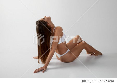 Portrait of young beautiful girl with long brunette hair posing in underwear over grey studio background. Concept of body and skin care, fitness Portrait of young beautiful girl with long brunette hair posing in underwear over grey studio background. Concept of body and skin care, fitness 98325698