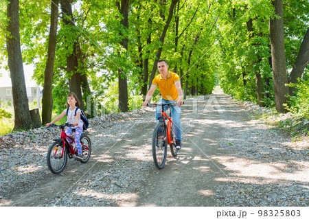 A father teaches his daughter to ride a bike. Family spending time together A father teaches his daughter to ride a bike. Family spending time together 98325803