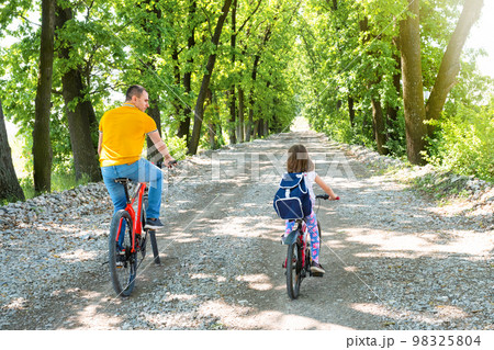 A happy dad with daughter ride bikes in the park. Back view 98325804