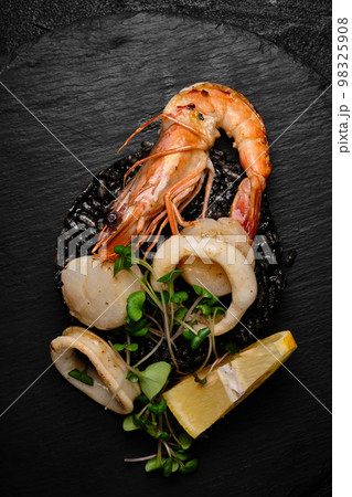 black risotto with crayfish, squid rings and scallop on a black plate on a black concrete background 98325908