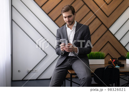 businessman sitting on the desk in the office reading messages on the phone 98326021
