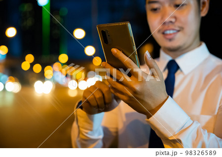 Young man walking and chatting on mobile phone with friends at social networks outdoor, Portrait Asian businessman typing an sms message via smartphone after work near office at night city street 98326589