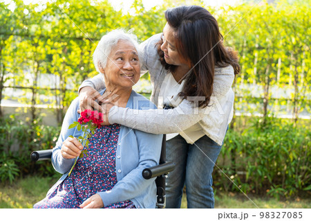 Caregiver daughter hug and help Asian senior or elderly old lady woman holding red rose on wheelchair in park. Caregiver daughter hug and help Asian senior or elderly old lady woman holding red rose on wheelchair in park. 98327085