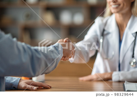 Doctor Woman Wearing White Coat Shaking Hands With Male Patient In Clinic Doctor Woman Wearing White Coat Shaking Hands With Male Patient In Clinic 98329644