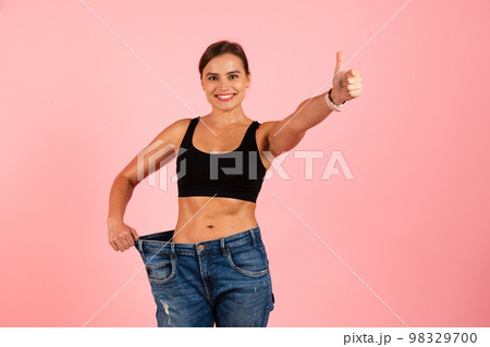 Successful Diet. Happy Slim Woman Wearing Oversized Jeans And Showing Thumb Up Successful Diet. Happy Slim Woman Wearing Oversized Jeans And Showing Thumb Up 98329700