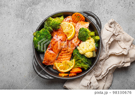 Healthy baked fish salmon steaks, broccoli, cauliflower, carrot in black cast iron casserole bowl on grey rustic stone background. Cooking a delicious low carb dinner, healthy nutrition concept 98330676