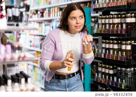 Satisfied young woman chooses and tries perfume in cosmetics store Satisfied young woman chooses and tries perfume in cosmetics store 98332856