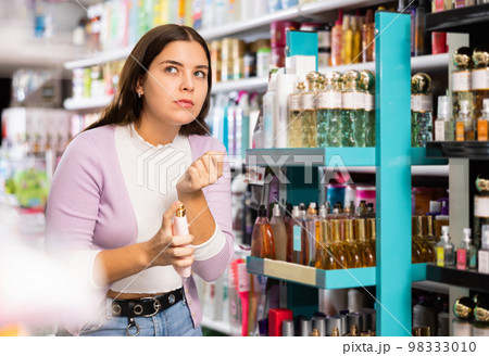 Satisfied young woman chooses and tries perfume in cosmetics store Satisfied young woman chooses and tries perfume in cosmetics store 98333010