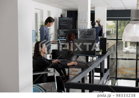 Asian disabled software programmer writing html code in agency big data room, using security system. Engineer with physical disability programming user interface artificial intelligence office. 98333238