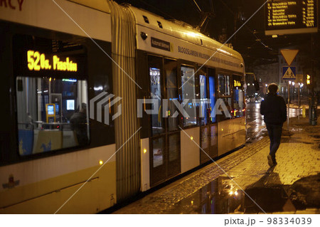 A tram in the night city travels around Krakow with timetable. Man alone walking near the tram. A tram in the night city travels around Krakow with timetable. Man alone walking near the tram. 98334039