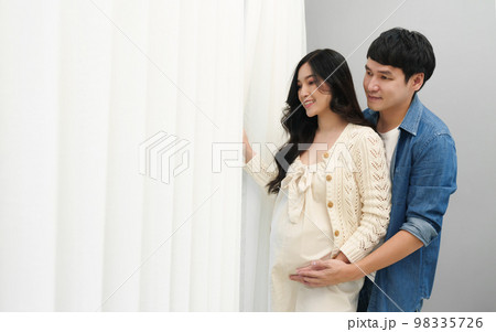 married couple is expecting baby. man embracing and talking with his pregnant wife while looking view through the window 98335726
