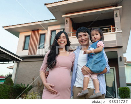 happy family standing outside house, husband and pregnant wife and baby girl 98335727
