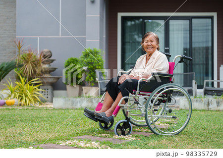 happy senior woman in wheelchair at outside the house 98335729