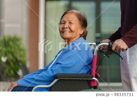 grandson pushing happy senior woman in wheelchair at outside house 98335731
