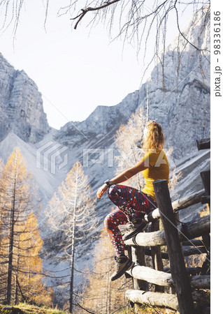 Vertical photo of unrecognizable woman hiker sitting on a wooden fence somwhere in the autumn mountains 98336186