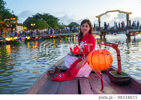 woman wearing Ao Dai Vietnamese dress, traveler Sightseeing Boat Ride and floating paper lantern at Hoi An ancient town. landmark for tourist attractions.Vietnam and Southeast travel concept 98338655