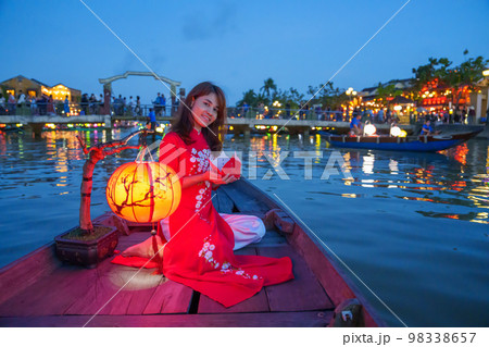woman wearing Ao Dai Vietnamese dress, traveler Sightseeing Boat Ride and floating paper lantern at Hoi An ancient town. landmark for tourist attractions.Vietnam and Southeast travel concept 98338657
