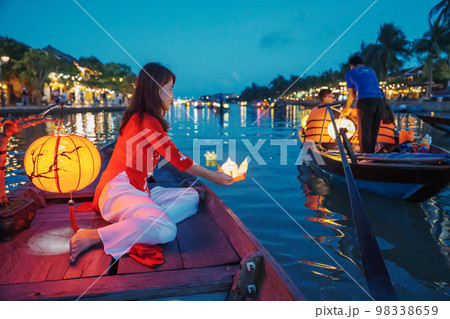 woman wearing Ao Dai Vietnamese dress, traveler Sightseeing Boat Ride and floating paper lantern at Hoi An ancient town. landmark for tourist attractions.Vietnam and Southeast travel concept 98338659