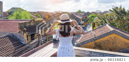 happy traveler traveling at Hoi An ancient town in Vietnam, woman with dress and hat sightseeing view at rooftop.landmark and popular for tourist attractions. Vietnam and Southeast Asia travel concept 98338821