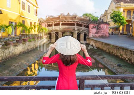 Woman traveler wearing Ao Dai Vietnamese dress sightseeing at Japanese covered bridge in Hoi An town, Vietnam. landmark and popular for tourist attractions. Vietnam and Southeast Asia travel concept 98338882