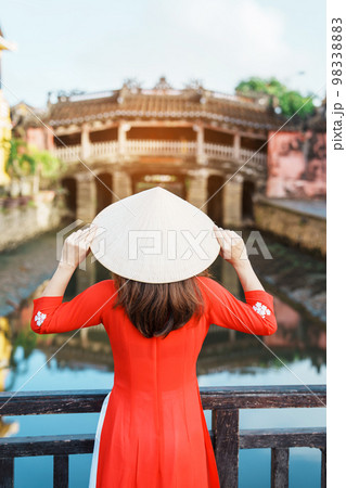 Woman traveler wearing Ao Dai Vietnamese dress sightseeing at Japanese covered bridge in Hoi An town, Vietnam. landmark and popular for tourist attractions. Vietnam and Southeast Asia travel concept 98338883