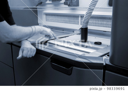 A male worker stands near the powder part of a powder 3D printer and points his finger of the hand at it. industrial production equipment. New modern 3D printing additive progressive technology MJF 98339691