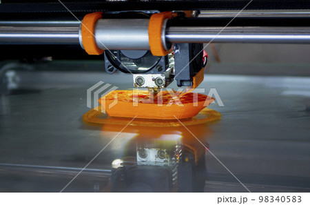 3d printer printing a model close-up. The process of printing a model on a 3D printer made of orange plastic. 3D printer working close up 3d printer printing a model close-up. The process of printing a model on a 3D printer made of orange plastic. 3D printer working close up 98340583
