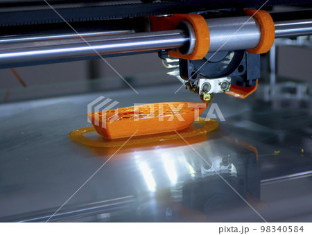 3d printer printing a model close-up. The process of printing a model on a 3D printer made of orange plastic. 3D printer working close up 3d printer printing a model close-up. The process of printing a model on a 3D printer made of orange plastic. 3D printer working close up 98340584